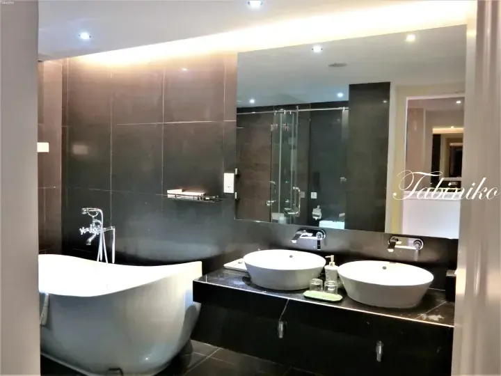 Modern luxury bathroom featuring a freestanding white bathtub, dual vessel sinks, and dark tiled walls with recessed lighting.