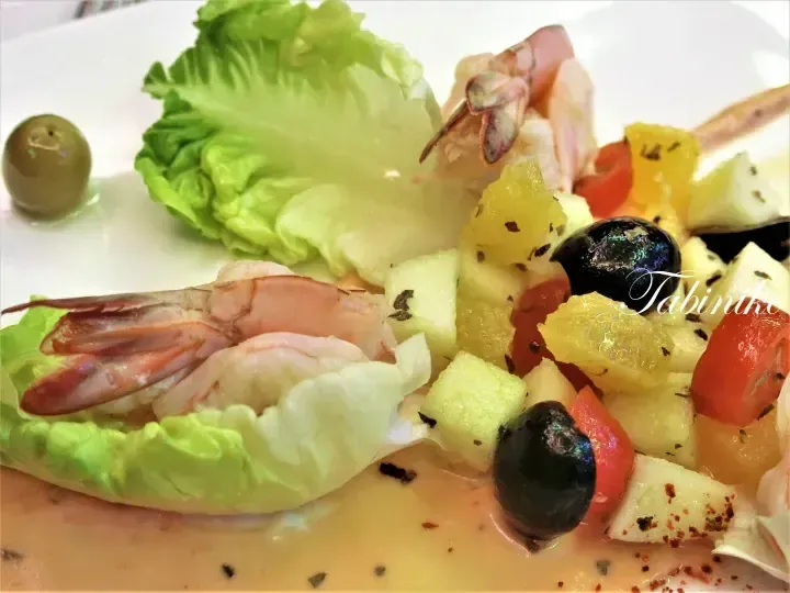 Fresh salad with prawns, lettuce, olives, and fruit chunks served on a white plate.