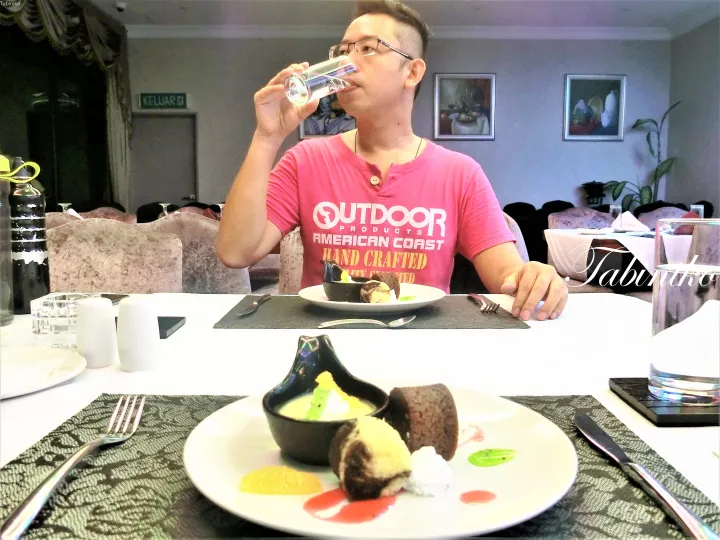 デザートが置かれたテーブルで、ピンクのシャツを着た男性が水を飲んでいるレストランのシーン。