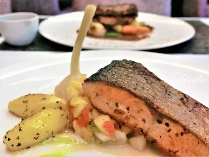 Pan-seared salmon fillet with crispy skin served on a bed of diced vegetables and garnished with herbs and sauce