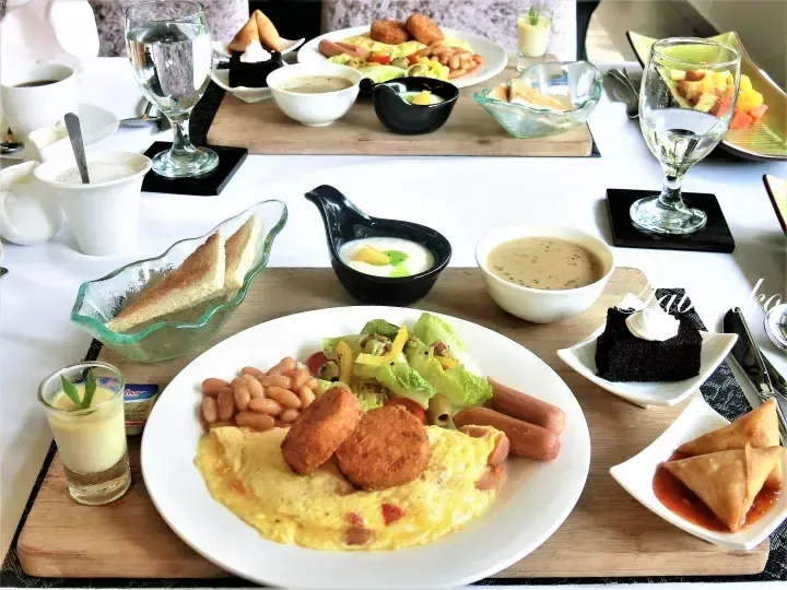 A lavish breakfast spread featuring omelets, sausages, beans, toast, and desserts on a white tablecloth.