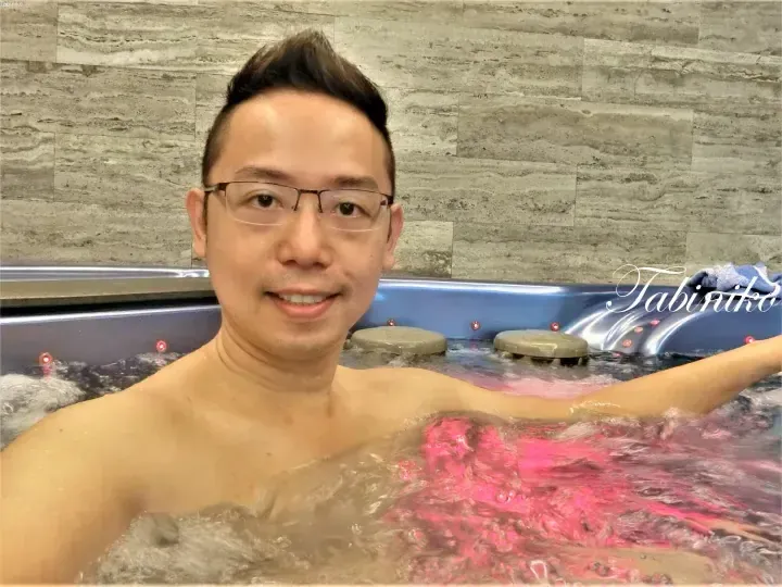 A man relaxes in a bubbling jacuzzi with pink lighting at a modern spa facility.