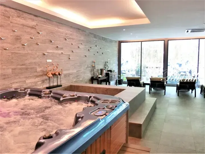 Indoor spa area with a bubbling hot tub, stone wall, and lounge chairs near large windows.
