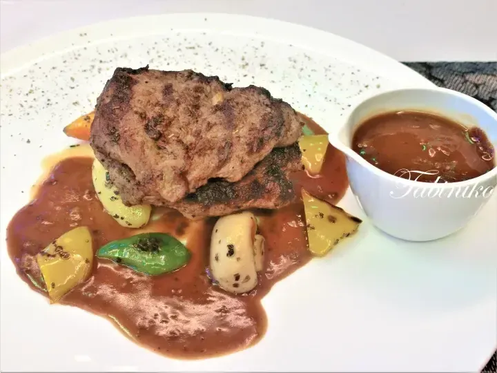 Grilled steak with vegetables and brown sauce served on a white plate with a side bowl of gravy.