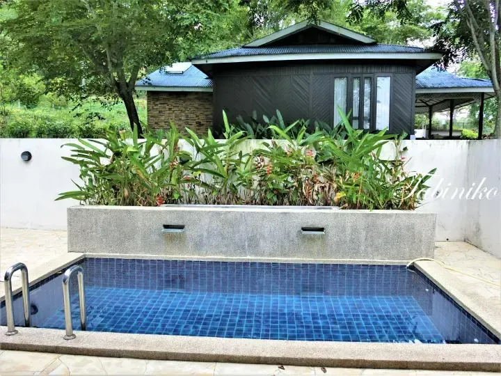 Private pool with blue tiles and waterfall feature at a resort villa surrounded by lush greenery