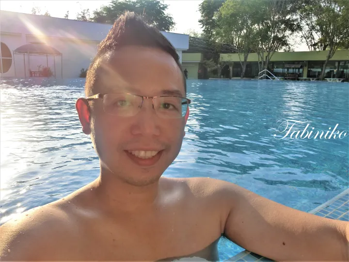 夕暮れのプールに映る笑顔の男性と、背景のリゾート施設。