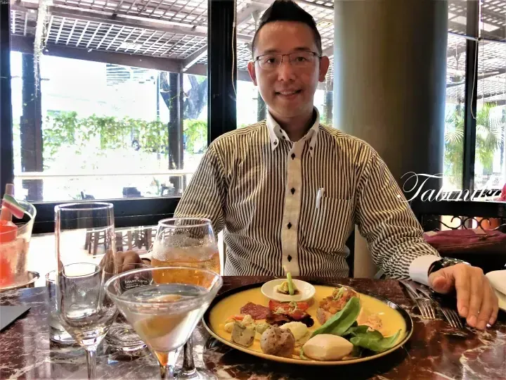 Man in striped shirt dining at a restaurant with a charcuterie platter and drinks on a marble table.