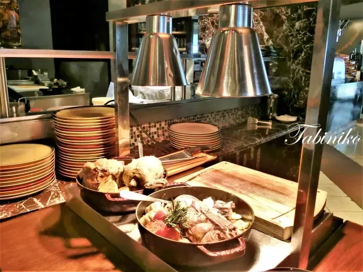 Buffet station with roasted chicken and meat dishes under heat lamps, with stacks of plates ready for guests.