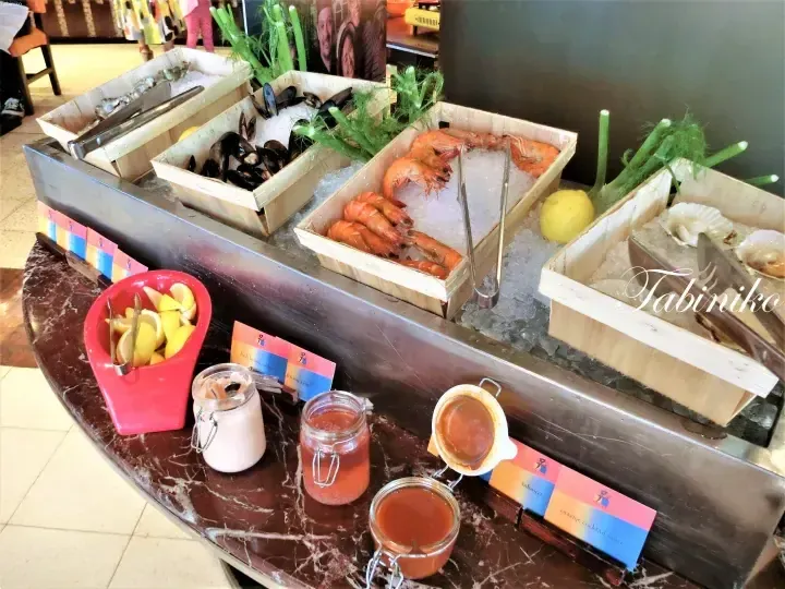 Fresh seafood buffet display featuring prawns, mussels, and scallops on ice with dipping sauces and lemon wedges.