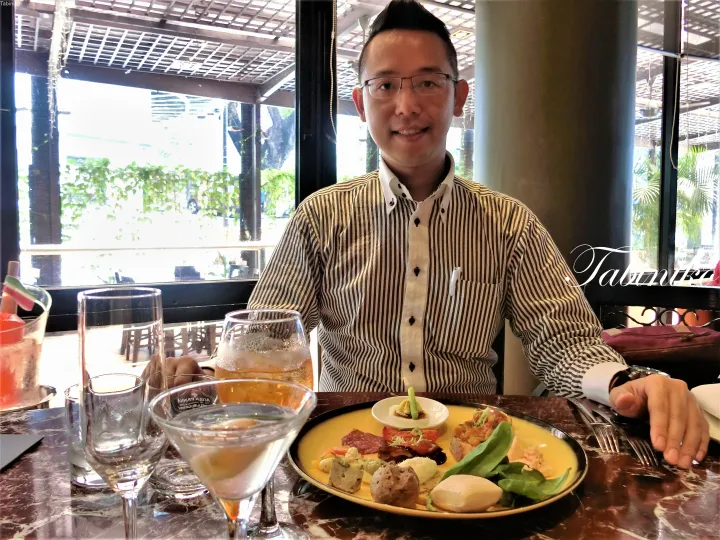 大理石のテーブルでシャルキュトリープレートとドリンクを前に食事をするストライプシャツの男性。
