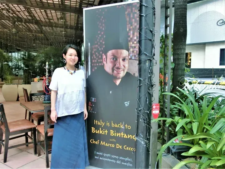 Woman posing next to a poster for Chef Marco De Cecco at a restaurant in Bukit Bintang.