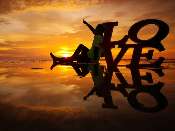 夕焼けのビーチに座り、大きなLOVEの文字と反射を楽しむ人物のシルエット。