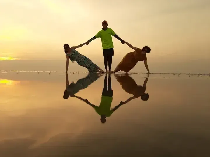 Three people pose on the reflective surface of a salt flat at sunset, creating a perfect mirror image.