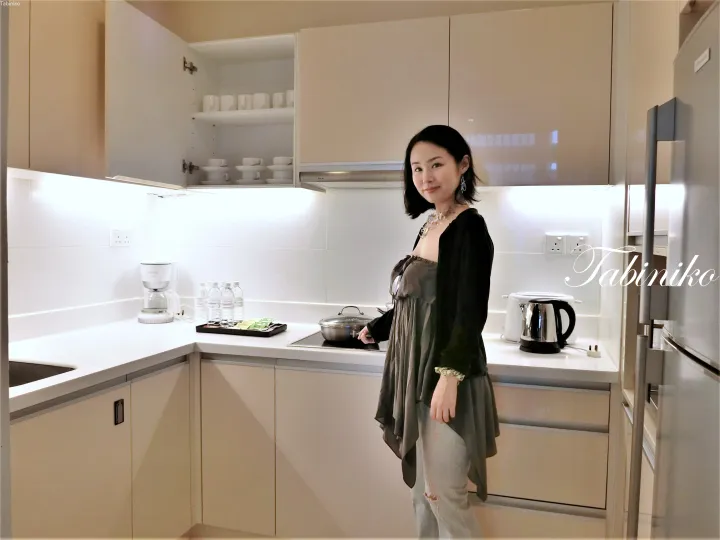 白いカウンターとベージュのキャビネットが特徴的なモダンなキッチンに立つ女性。