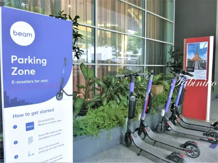 Beam e-scooter parking zone sign with instructions and parked scooters outside a building.