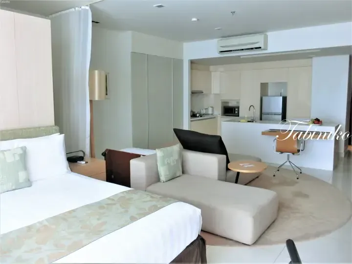 Modern hotel suite interior with a bed, sofa, and fully equipped kitchenette area.