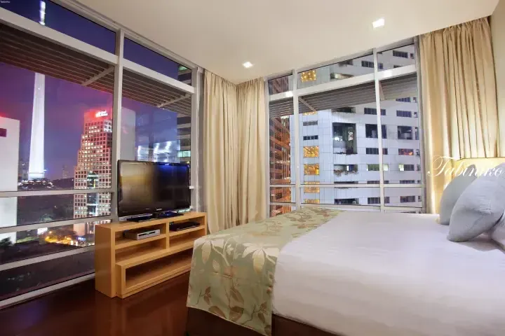 Modern hotel room with a large window overlooking Kuala Lumpur’s city skyline at night.