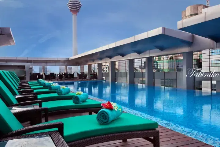 Rooftop pool with green loungers and towels overlooking Kuala Lumpur Tower