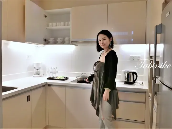 Woman standing in a modern kitchen with white countertops, beige cabinets, and a coffee maker.