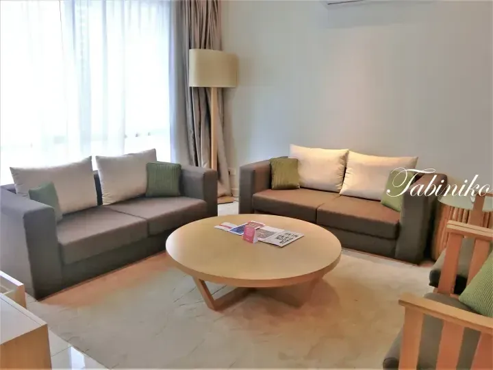 Modern hotel living room with grey sofas, green cushions, and a round wooden coffee table.