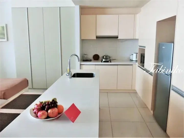 Modern kitchen with white cabinetry, island sink, and fruit plate in a serviced apartment.