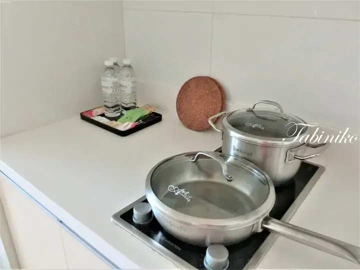 Ariston gas stove with stainless steel pots and a tray of water bottles on a white kitchen countertop.