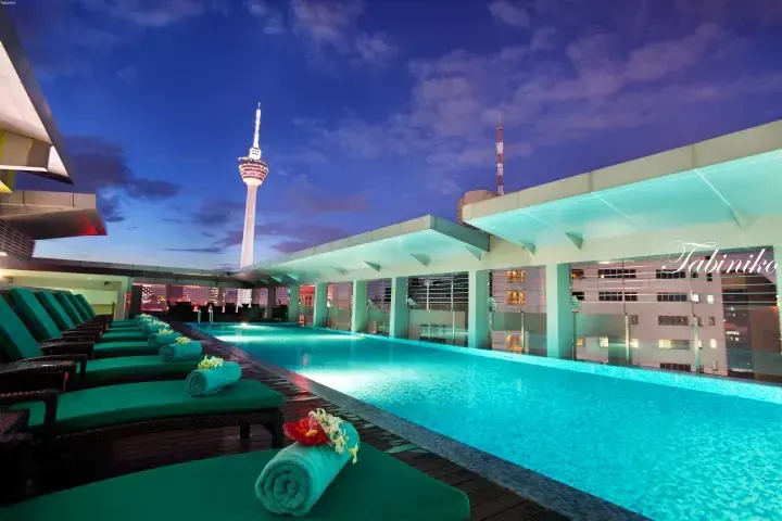 Rooftop infinity pool with lounge chairs and Kuala Lumpur Tower view at dusk