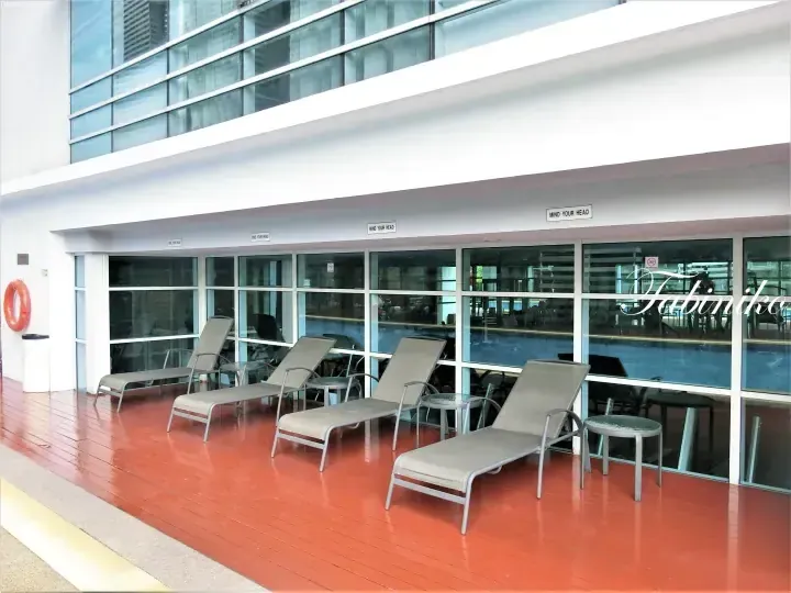 Outdoor pool deck with lounge chairs and red flooring beside glass windows at a Malaysia hotel