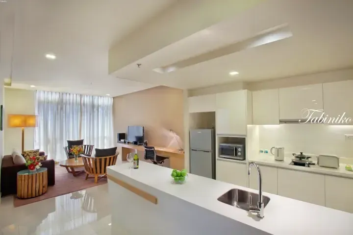 Modern serviced apartment interior featuring a white kitchen island, living area with sofa, and built-in appliances.