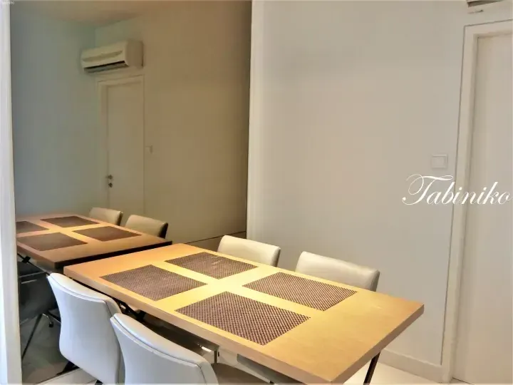 Modern dining area with wooden tables, white chairs, and woven placemats in a bright room.