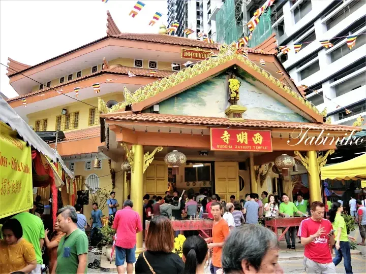 Buddha Jayanti Temple in Kuala Lumpur with devotees praying and colorful Buddhist flags decorating the entrance.