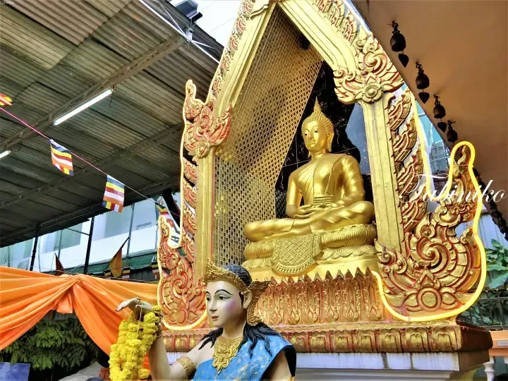 Golden Buddha statue seated in ornate shrine with marigold garlands and Buddhist flags at a Malaysian temple.