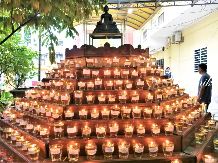 マレーシアの寺院で、仏像の下に段状の棚に並べられた灯り続けるろうそく。