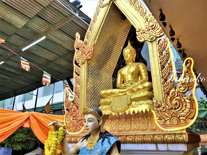 マレーシアの寺院にある金色の仏像と装飾的な祭壇、マーガレットの花輪と仏教旗。