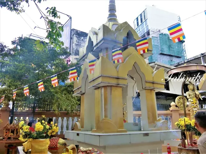 Golden Buddhist shrine adorned with colorful flags and yellow flowers, with a golden Buddha statue nearby.