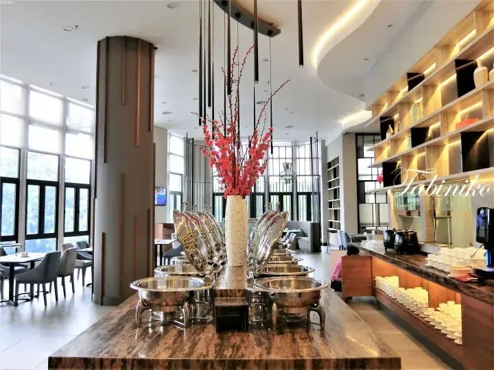 Modern buffet station with stainless steel chafing dishes and pink flowers in a bright hotel dining area