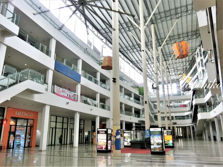 天井が高く白い柱が並ぶモダンな多層ショッピングモールの内部。MEDICOなどの店舗が見える。