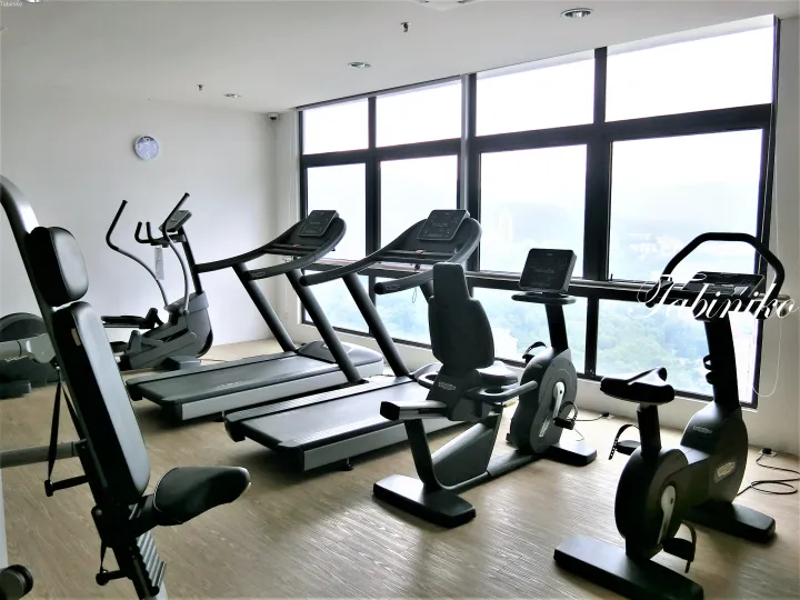 緑豊かな丘を望む大きな窓とTechnogymの設備を備えたモダンなジム