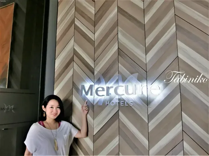 Woman posing next to the illuminated Mercure Hotels sign on a chevron-patterned wooden wall.