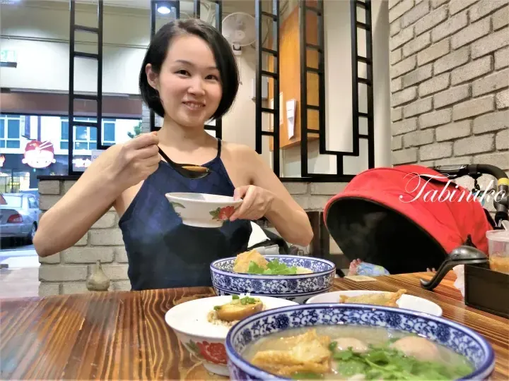 Woman enjoying a bowl of soup at a restaurant with blue and white patterned bowls and a red stroller nearby.