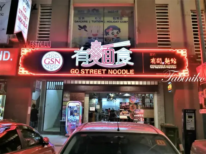 Go Street Noodle restaurant sign with red neon lights and Chinese characters at night.