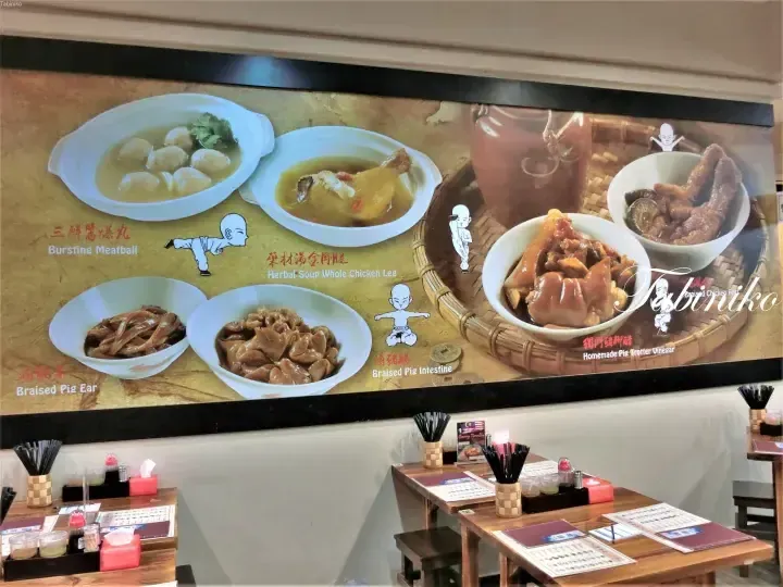 Wall menu displaying dishes like herbal soup chicken leg and braised pig intestine at a Malaysian restaurant.