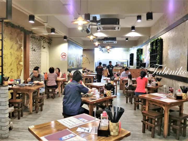 木製のテーブルと客席が並ぶレトロなレストランの店内。壁には禁煙標識があり、奥には厨房が見える。