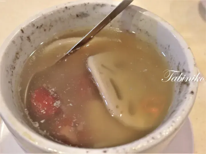 A close-up of a ceramic bowl containing a creamy soup with a dumpling and red ingredient, featuring a spoon and Tabiniko watermark.