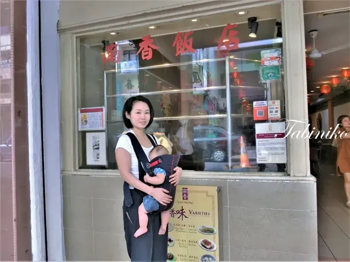 A woman holding a baby in a carrier stands outside Nam Heong restaurant in Kuala Lumpur, Malaysia.