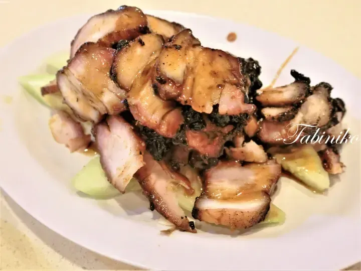 Sliced grilled pork belly with crispy edges served on a white plate with cucumber slices.