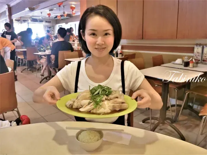 Woman holding a plate of Hainanese chicken rice at a restaurant in Malaysia.
