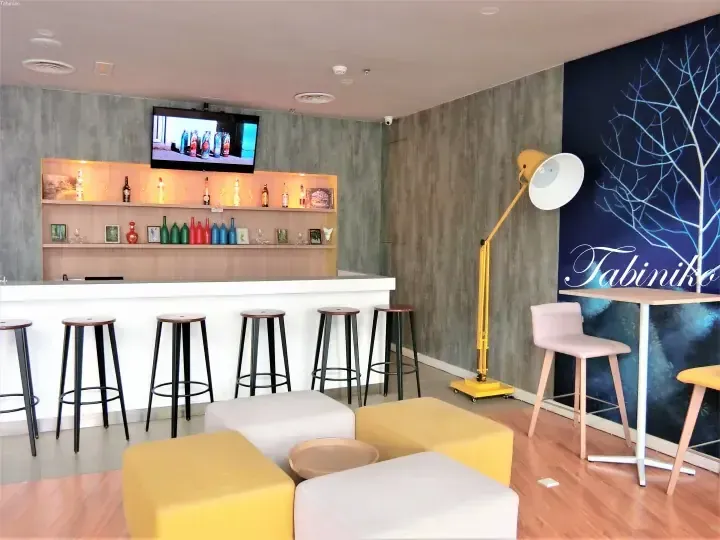 Modern hotel lounge with bar seating, yellow floor lamp, and blue tree mural at Tabiniko