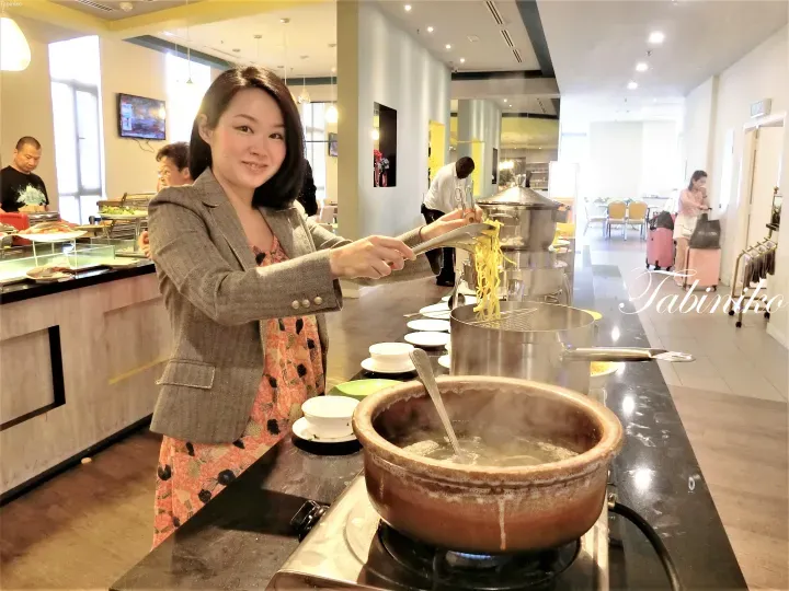 一名女子在明亮的餐廳自助餐台為麵條裝盤。