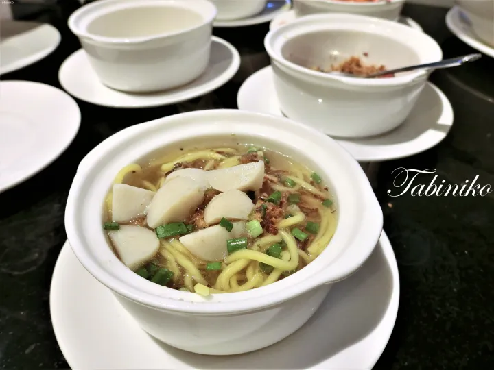 緑のネギを散らした魚肉団子と挽肉入りの麺料理が白い陶器のボウルに盛られている。